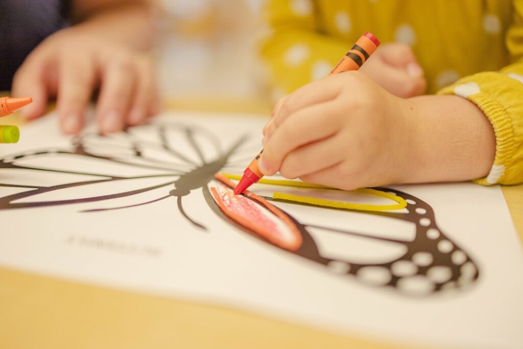 A child's hand coloring a butterfly with crayons