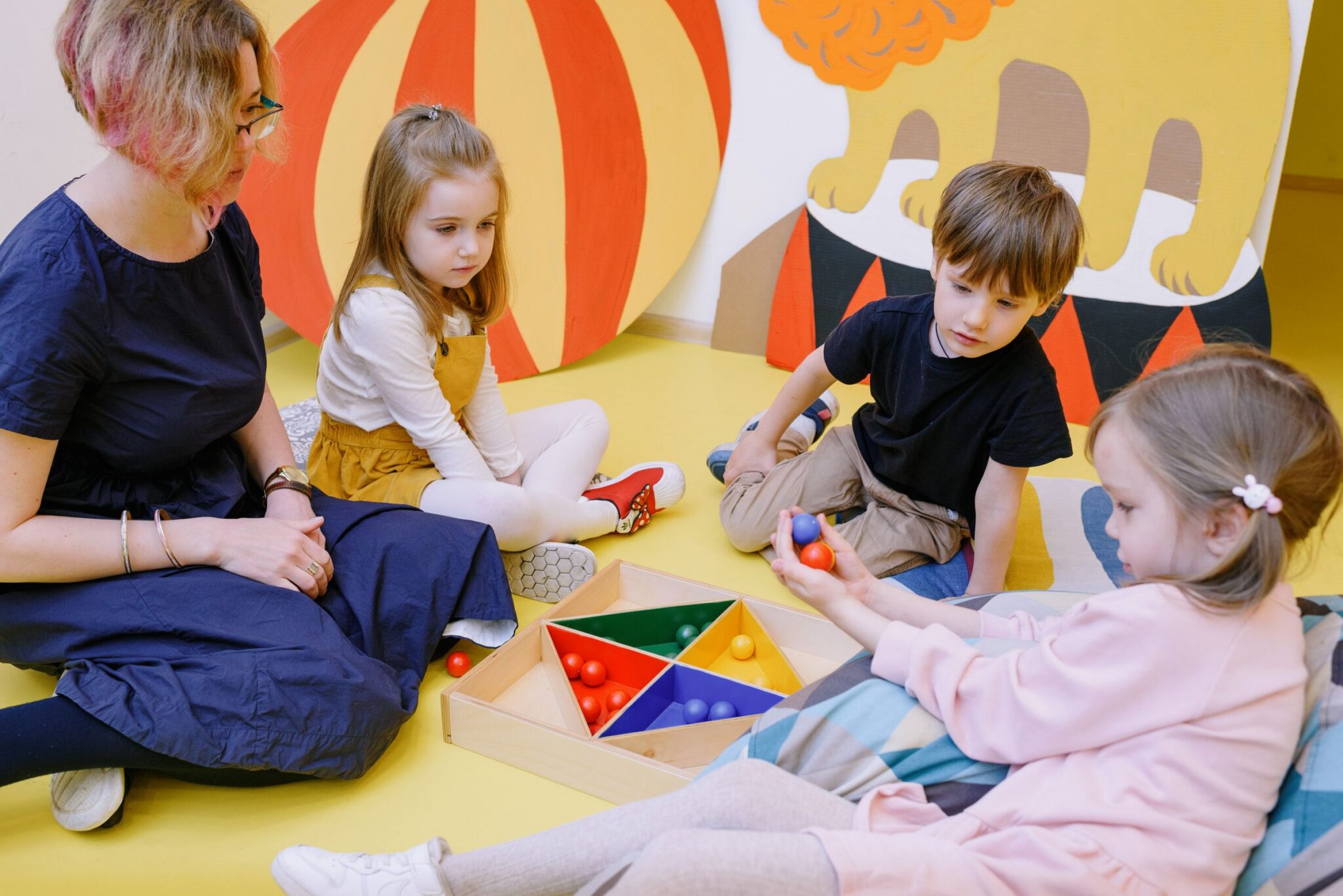 Children playing with colorful sorting toys alongside a teacher